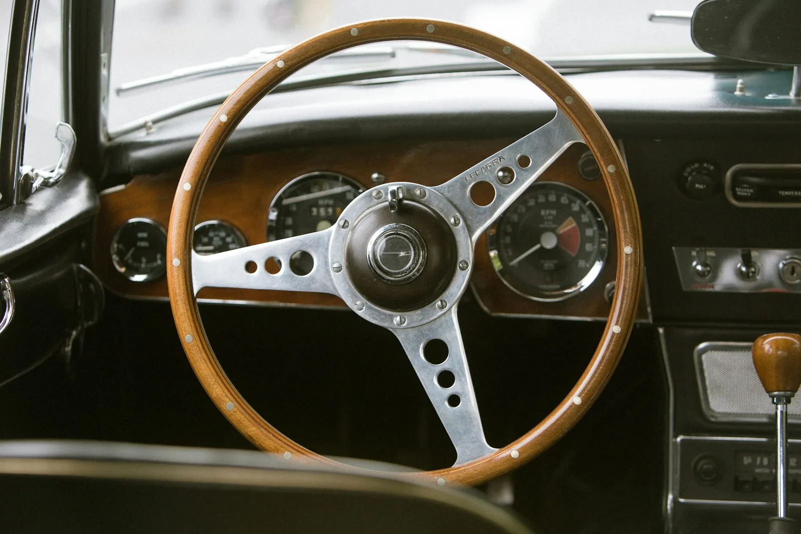 A wood-rimmed steering wheel and dash gauges in a classic car